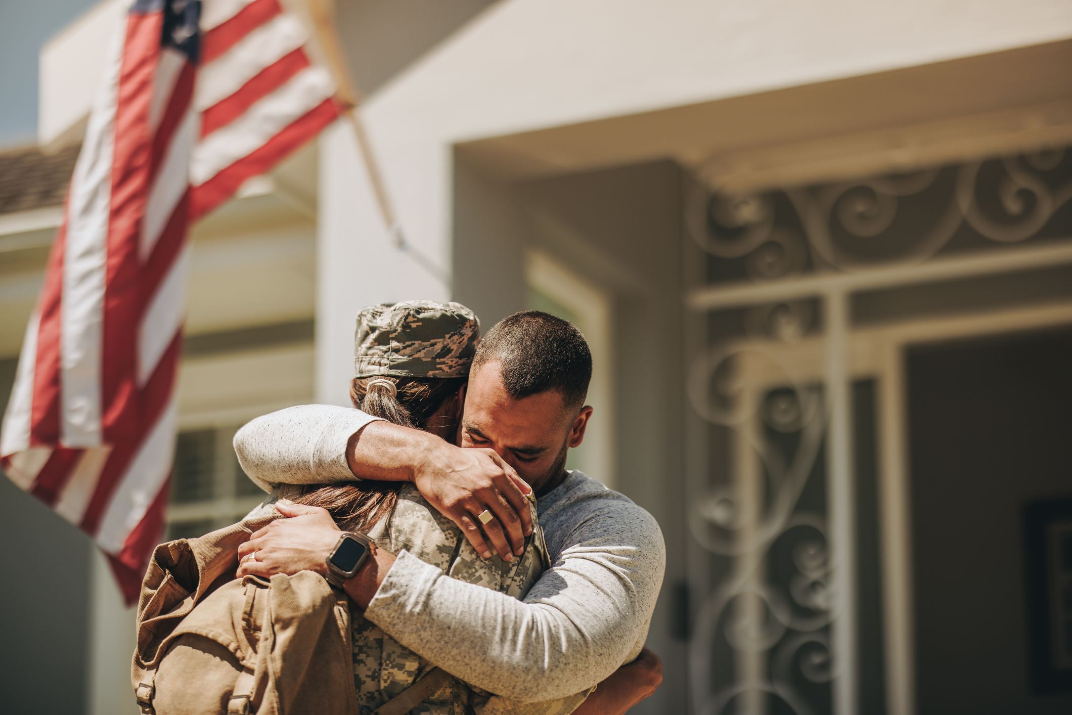 Military member comes home to her husband in an emotional display with an American flag flying behind them
