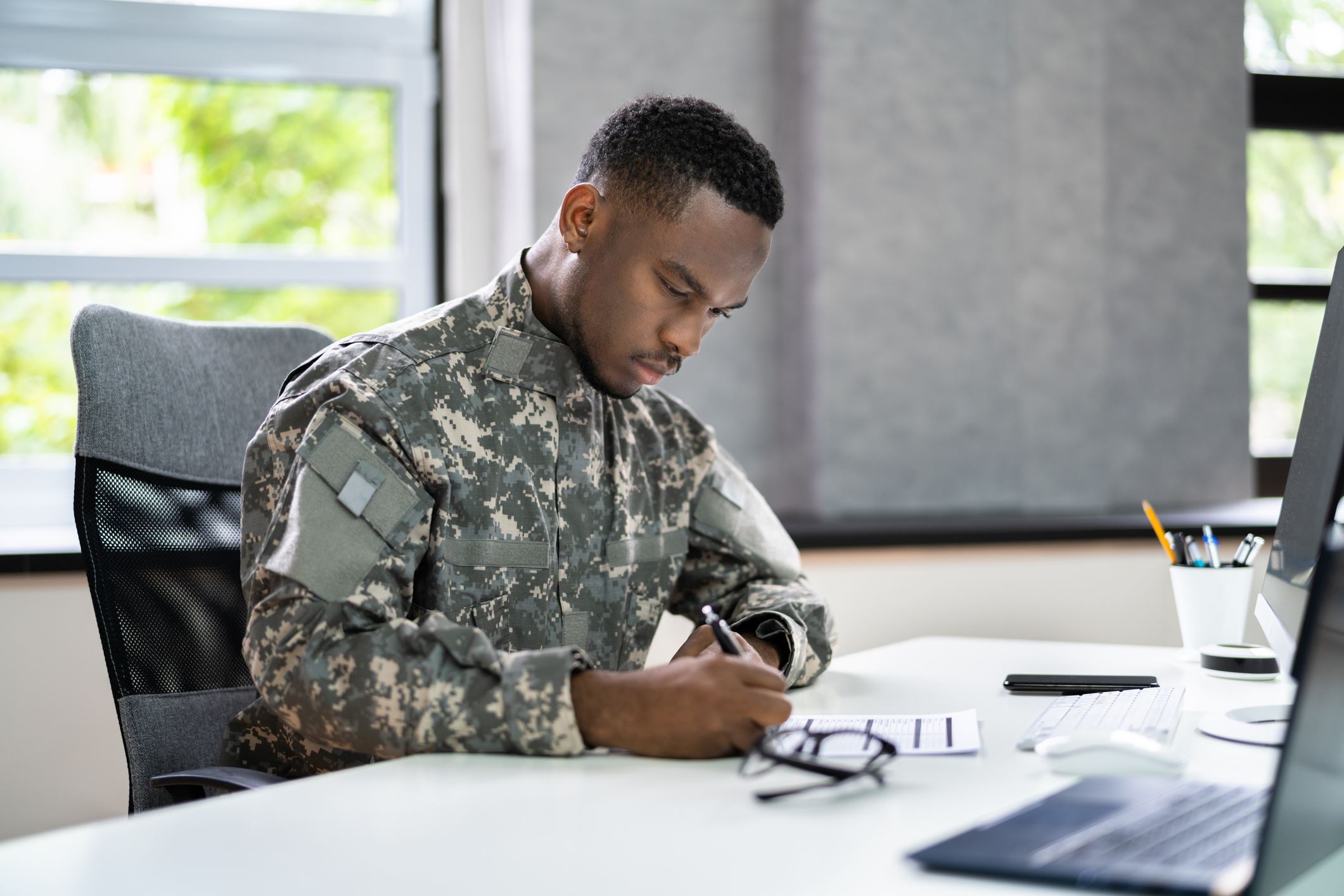 Military man writes on a document on a desk in an office